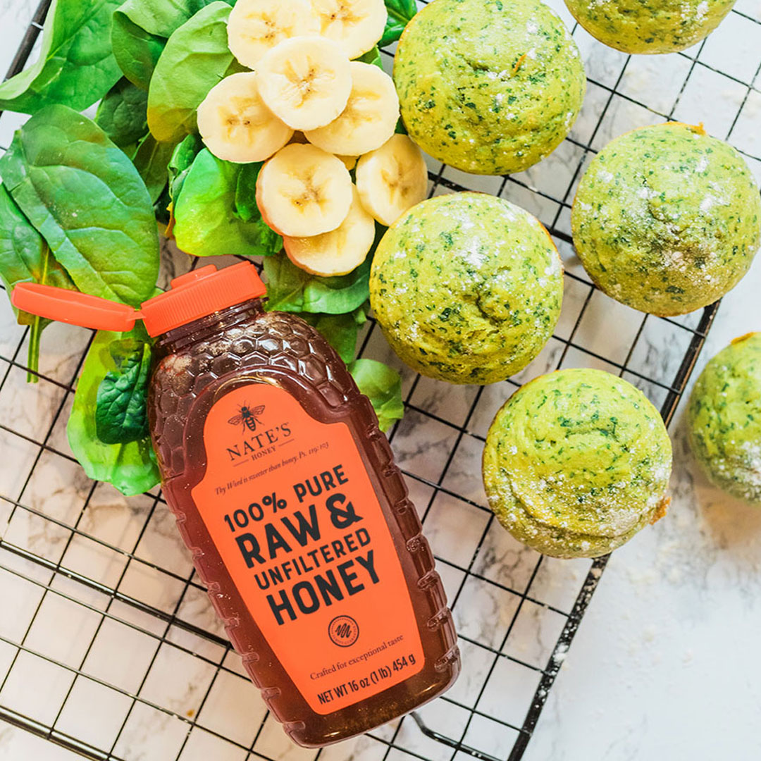 Spinach and banana muffins with Nate's Honey bottle on marble background.