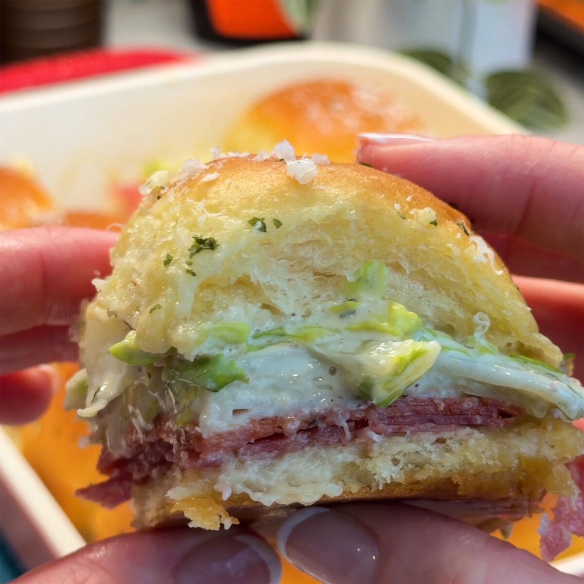 Hands holding one grinder sandwich layered with meat, cheese, veggies and honey on a Hawaiian roll.