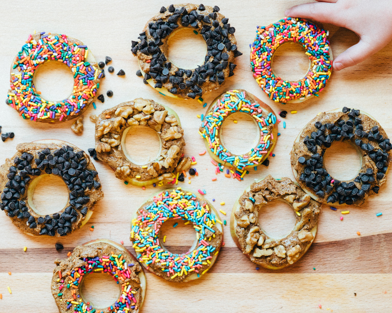 Hand reaching for donuts with chocolate chips, sprinkles, and nuts on wood.