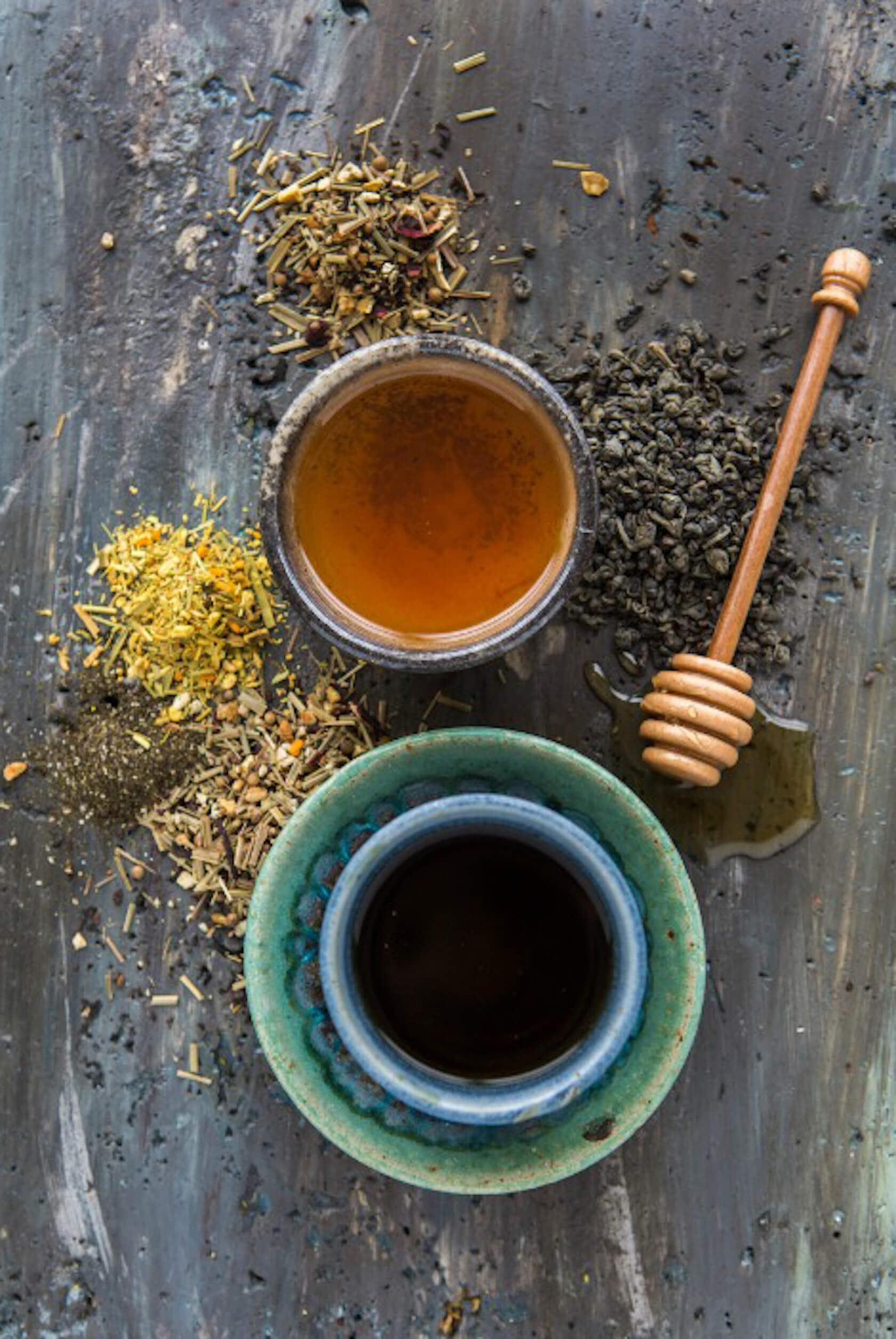 Loose tea leaves with honey in a small bowl and ceramic cups on a rustic wooden table.