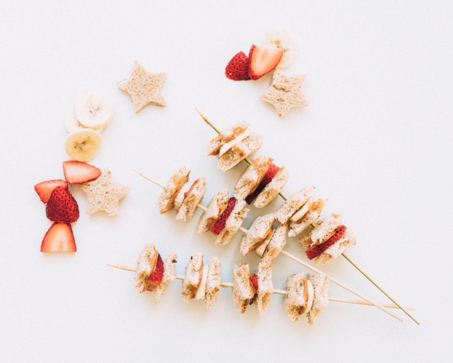 skewer with banana, strawberry, sandwich bites, and star-shaped toast on white platter.