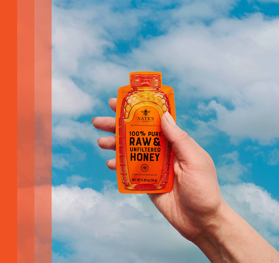 Hand holding Nate's honey mini with a cloudy sky in the background.