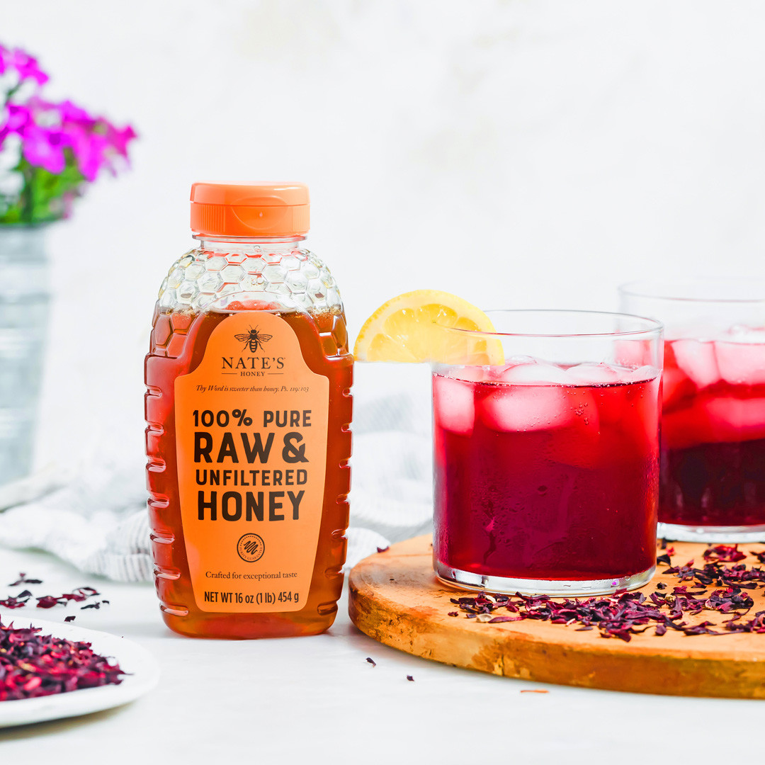 A bottle of Nate's Honey with two glasses of red spritzer and a lemon garnish on a table.
