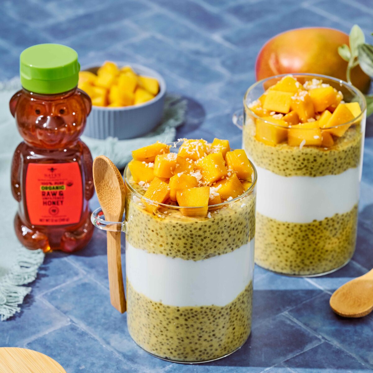 Glass mug filled with layered chia pudding topped with diced mango, shown with a wooden spoon.