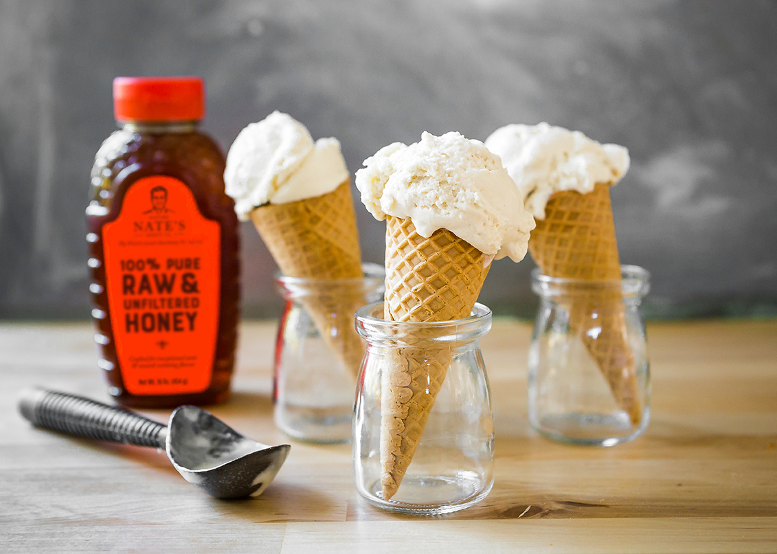 Vanilla ice cream cones in jars with honey bottle and scoop on a wooden table.