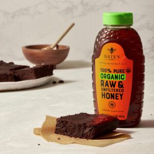 Brownies with a bottle of Nate's organic raw honey and a honey dipper in the background.