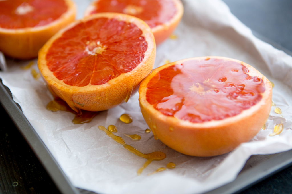 Four grapefruit halves on a baking sheet, drizzled with honey, on a parchment paper-lined tray.