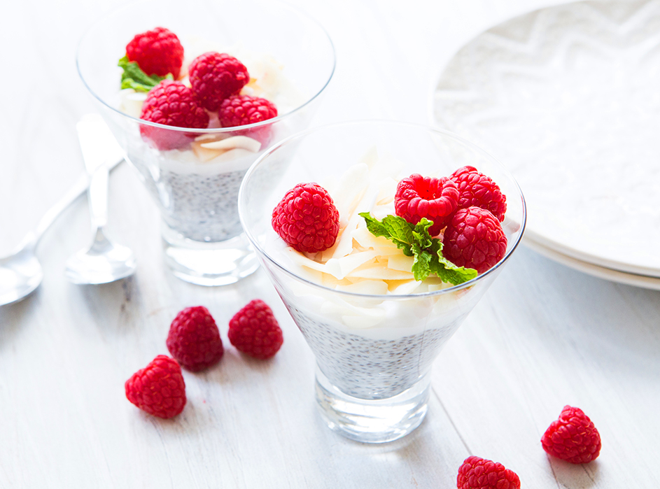 Two glasses of chia pudding topped with raspberries on a white textured surface.