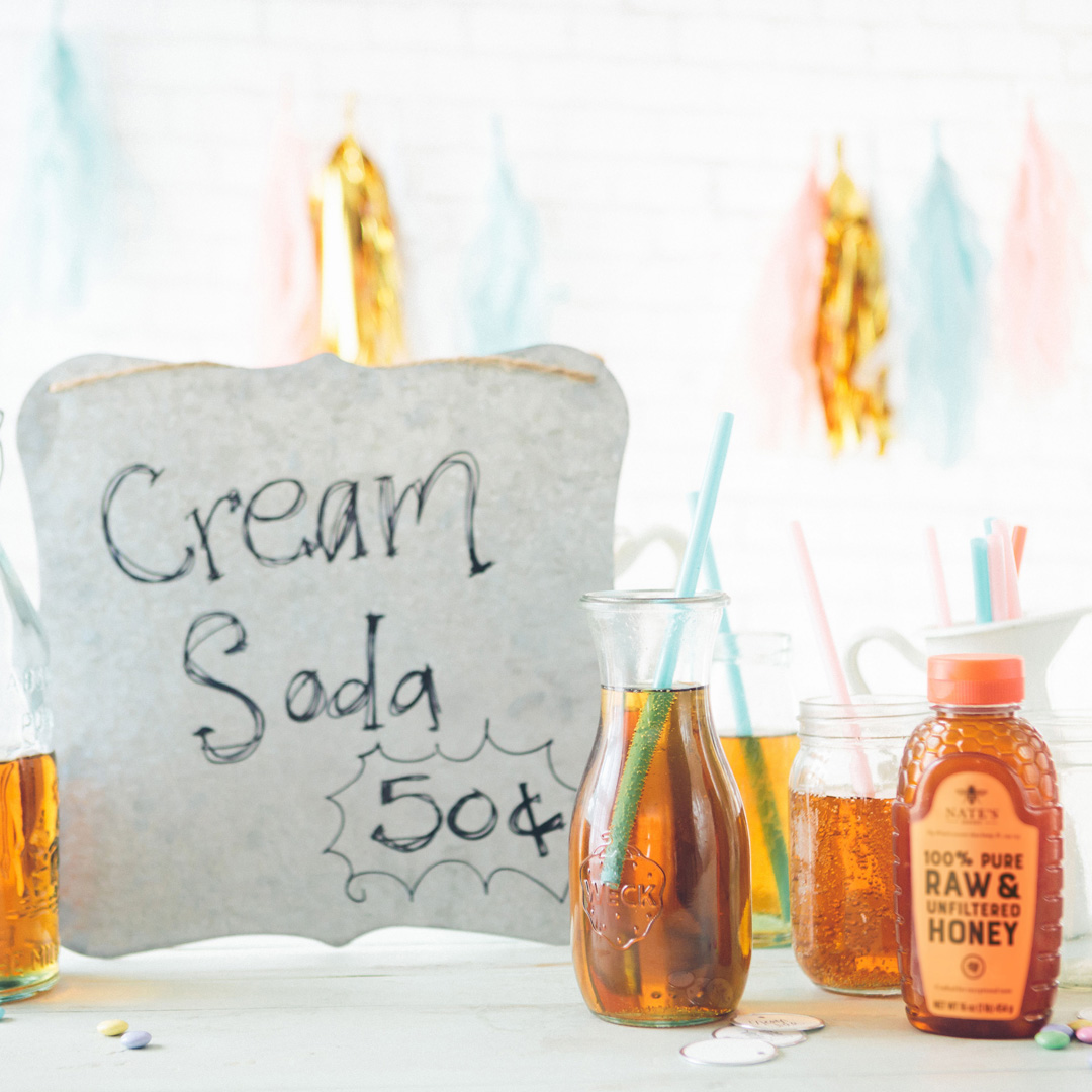 A festive setup with a Cream Soda 50¢ sign, bottles of drink, a Nate's Honey bottle, straws and confetti.