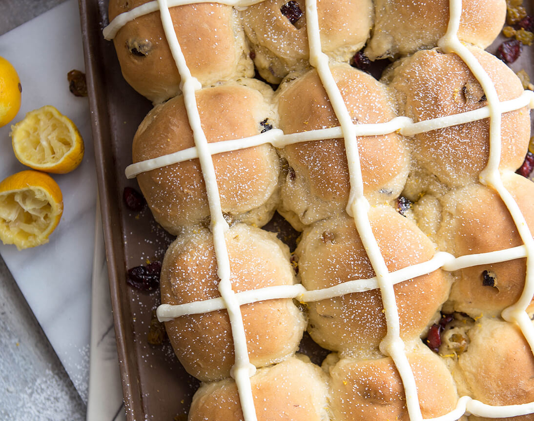 Hot cross buns with icing and dried fruit, on parchment, citrus in corner.
