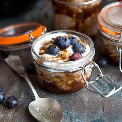 jar of honey bun overnight oats topped with blueberries on rustic background
