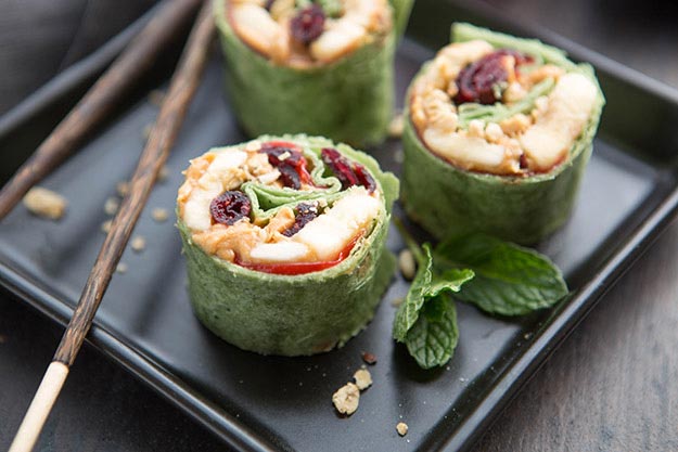 Peanut butter and fruit wrapped in a tortilla to look like sushi, on a black plate with chopsticks and mint.
