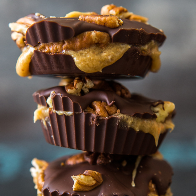 Three stacked chocolate nut butter cups with walnut topping, presented against a blurred background.