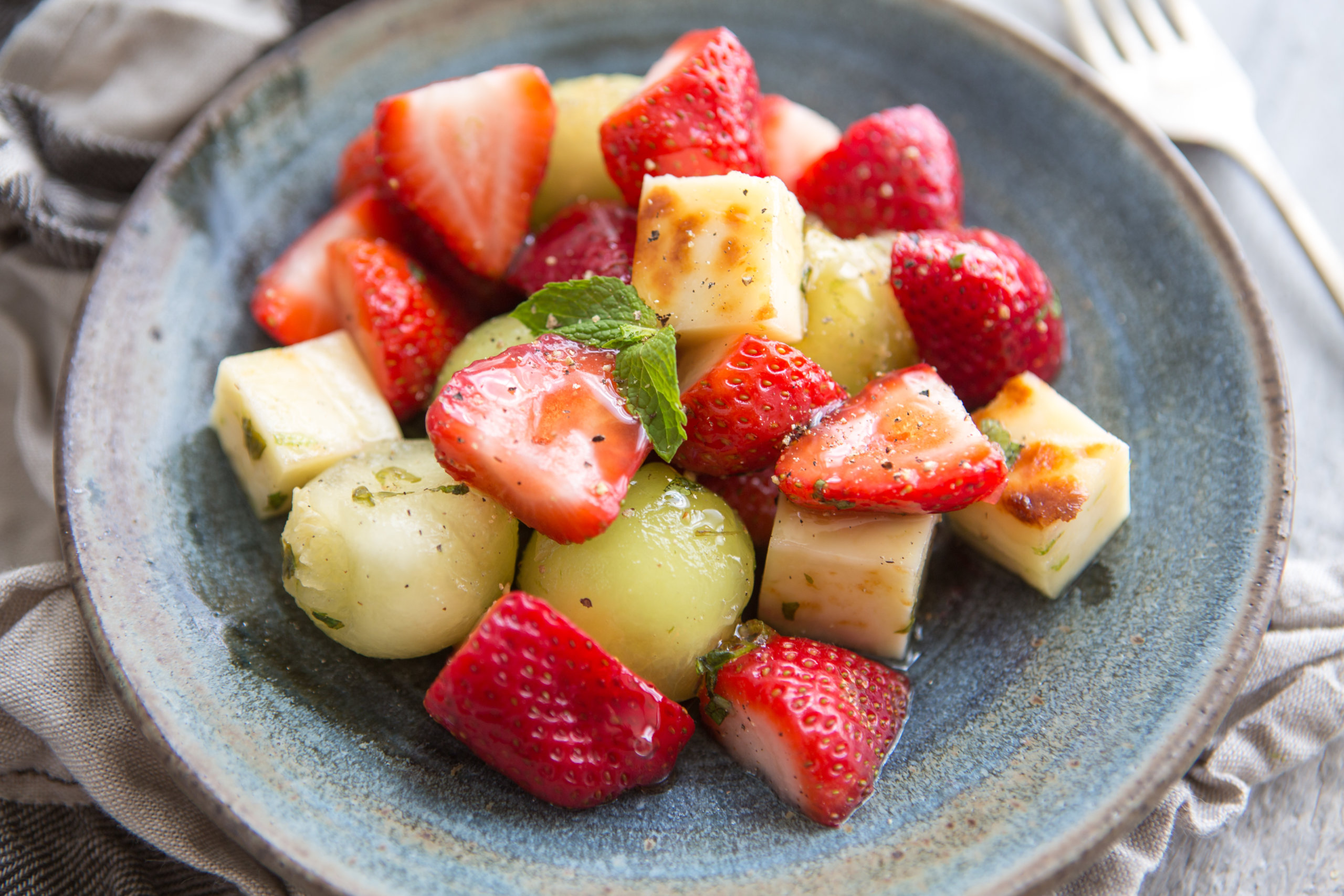 Colorful salad of fresh strawberries, melon balls, and cheese cubes, served on a rustic blue plate.