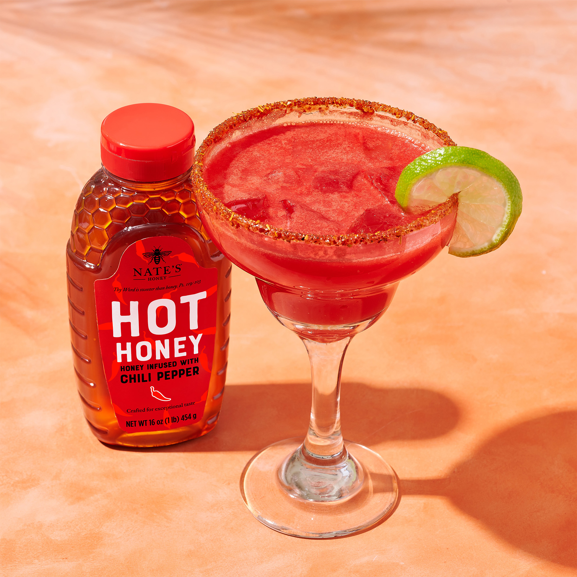 Pink margarita in glass next to hot honey bottle.
