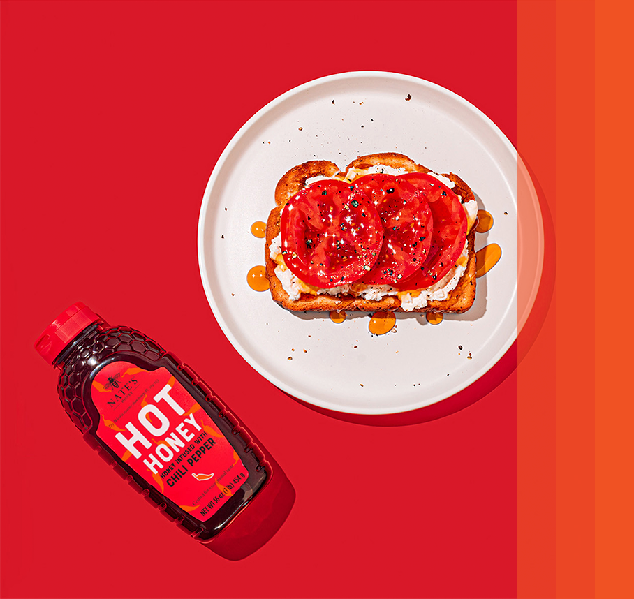 Tomato toast drizzled with hot honey on white plate with red background next to hot honey bottle.