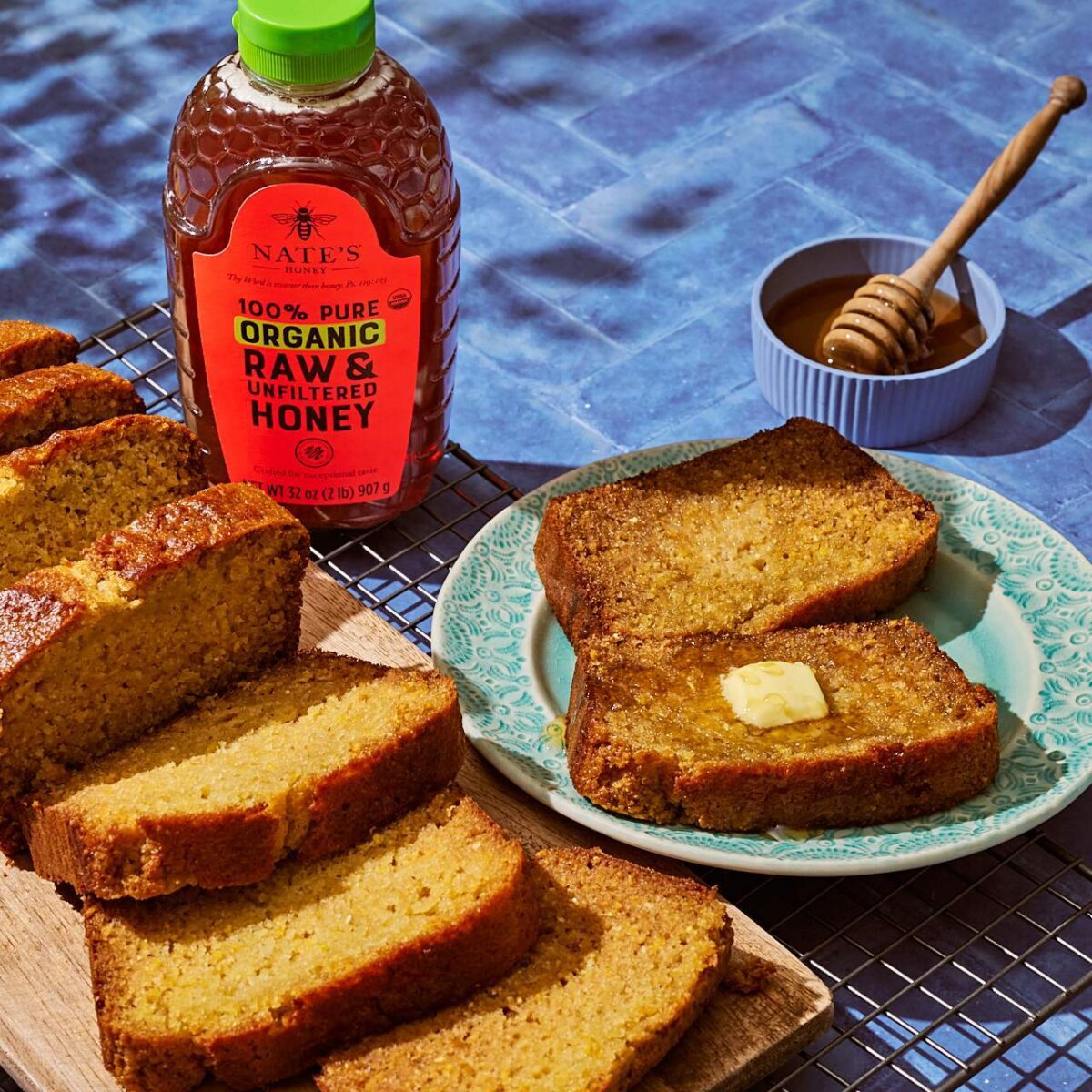 Slice of cornbread topped with a pat of butter and drizzled with honey on a blue patterned plate.