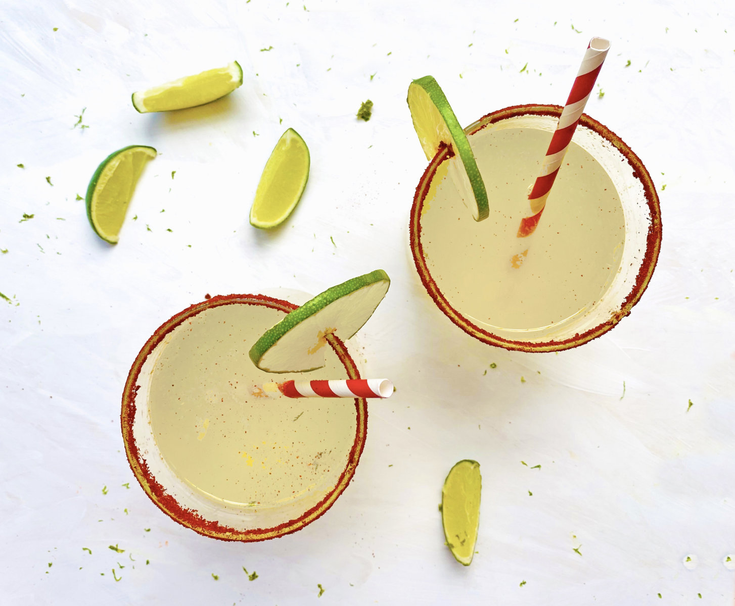 Two margaritas with lime wedges and chili-salt rims on a white surface.