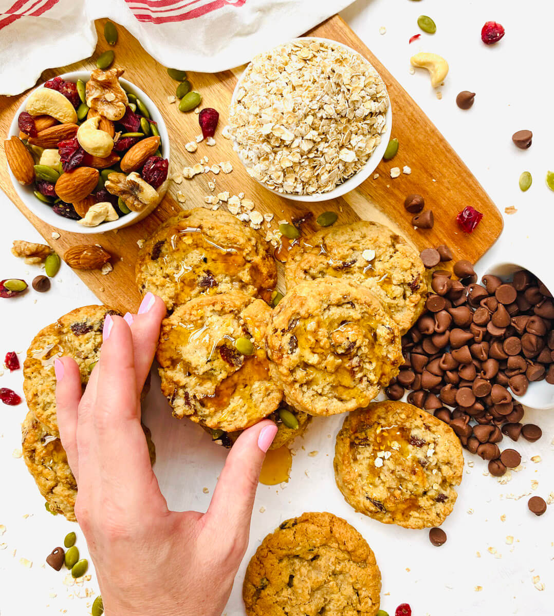 Hand picking up a cookie with nuts, chocolate chips and oats on a board.