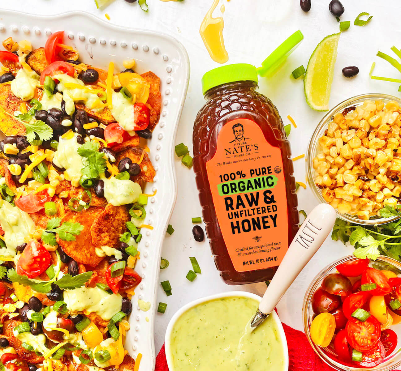 Sweet potato nachos with toppings, Nate's organic honey bottle, dip and roasted corn  on a white background.