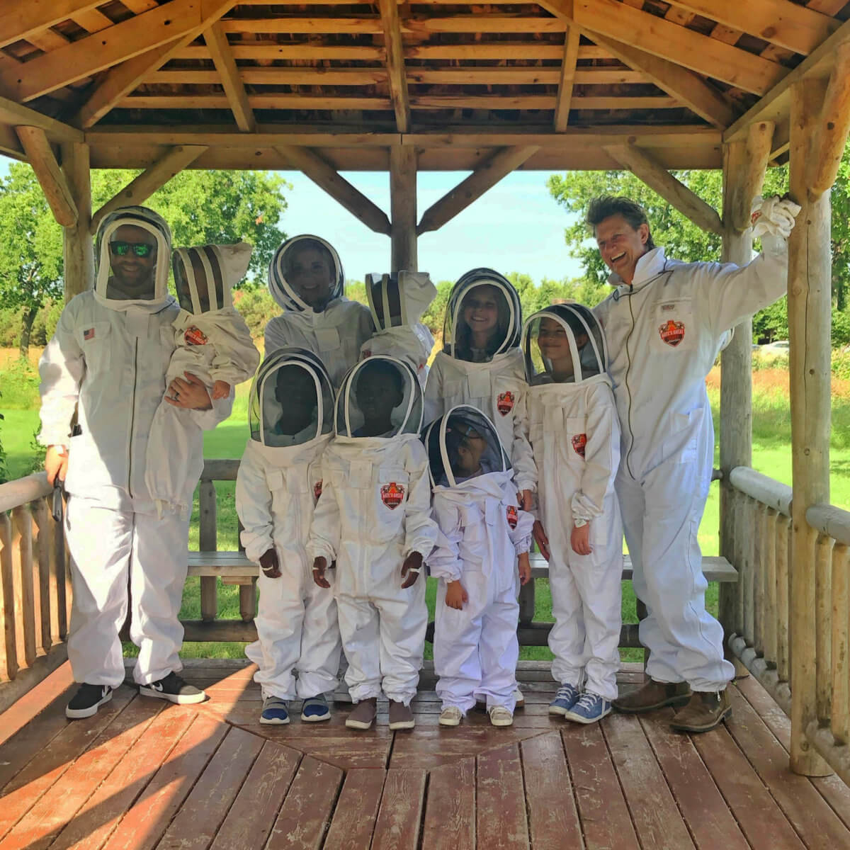 A group of people in beekeeping suits posing together in a wooden gazebo.