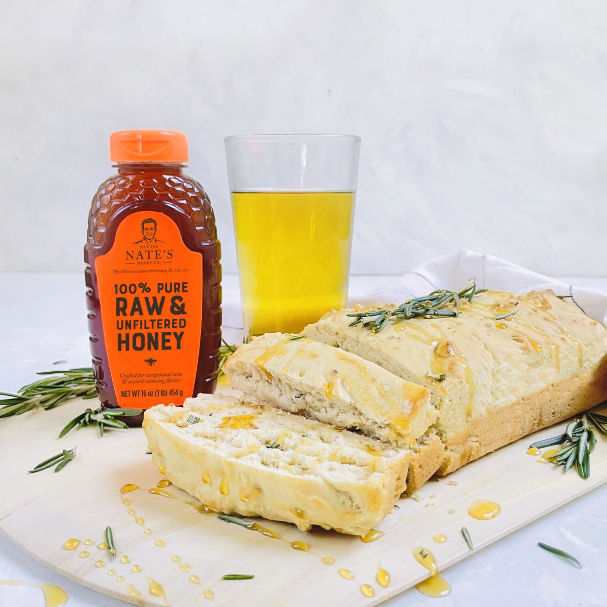 Beer bread on a board drizzled with honey and garnished with rosemary sprigs, a Nate’s honey bottle and a glass of beer.