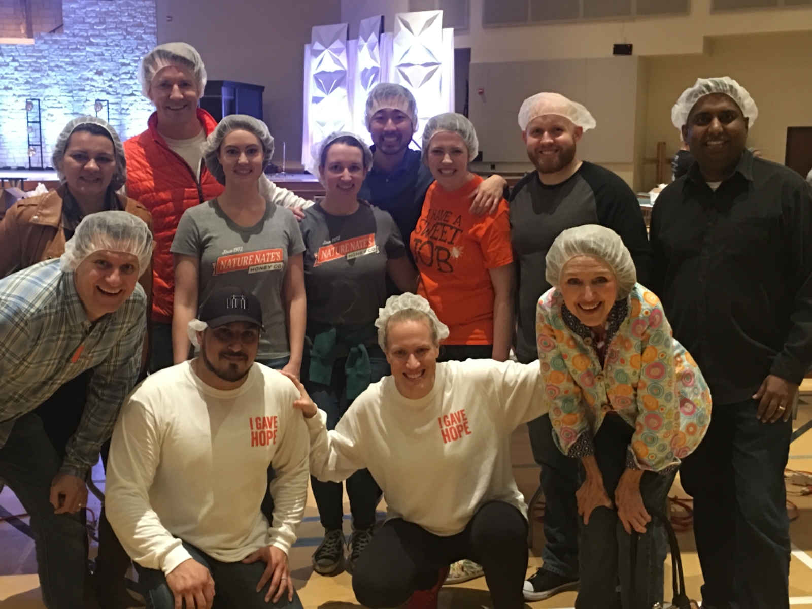 A group of cheerful people wearing hairnets and casual clothes, pose for a photo in an indoor setting.