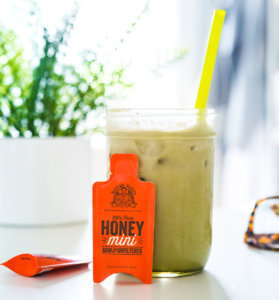 Iced matcha latte with a yellow straw and Nate's honey minis on a light background.