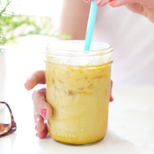 Hand holding a mason jar with iced turmeric milk and a blue straw.