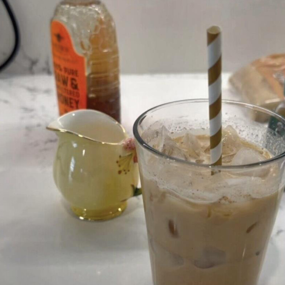 Teddy Graham Latte in clear glass cup with a bottle of Nate's honey in the background.