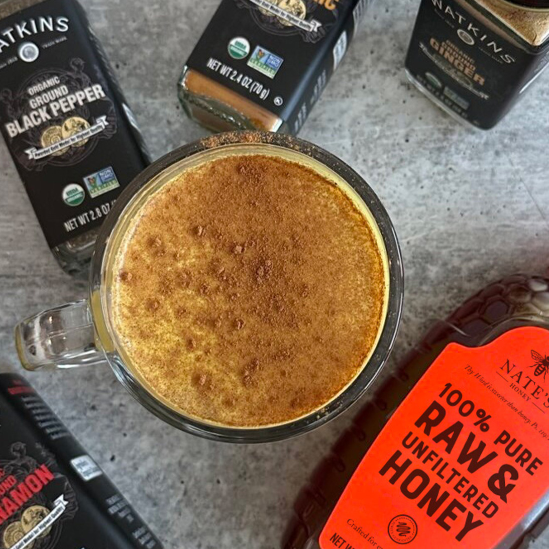 A spiced latte surrounded by Watkins organic spices and Nate's classic honey.