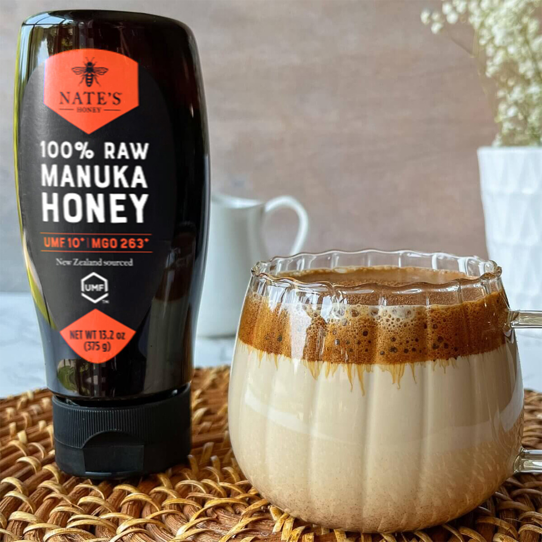 Clear pumpkin shaped mug filled with a pumpkin spice latte displayed next to Nate's Manuka Honey.