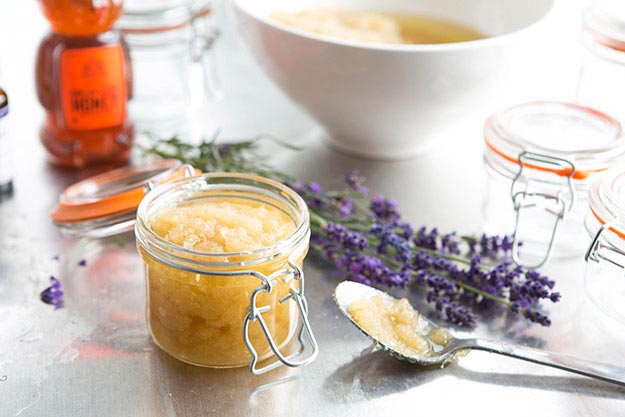 Jar of homemade honey and lavender sugar scrub, lavender sprigs, and Nate's honey bottle on a light, hazy tabletop.