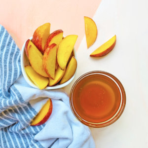 Sliced peaches on a blue striped cloth with a bowl of honey.