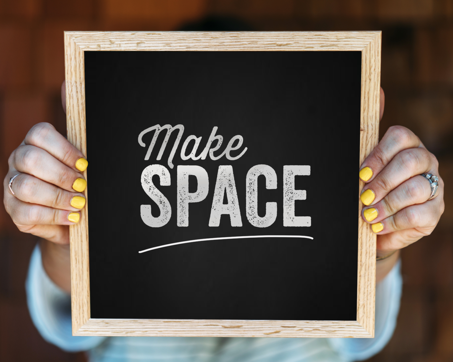 Person holding a chalkboard sign with Make SPACE written on it.