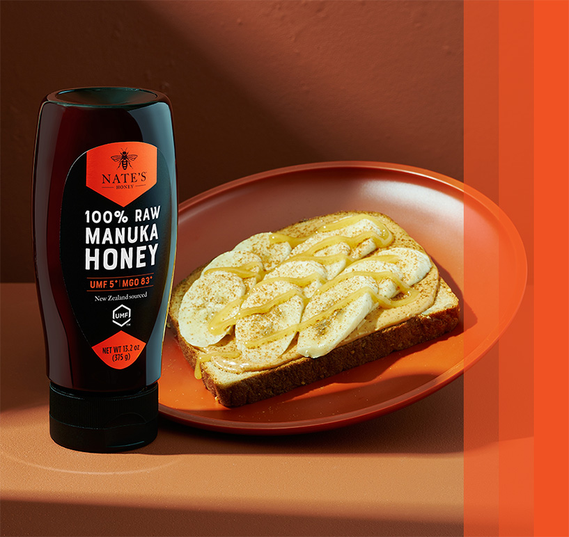 Nate's New Zealand Manuka Honey bottle beside a plate with honey-drizzled toast topped with banana slices.