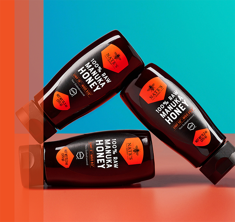 3 bottles of Manuka honey sitting on red table with blue backdrop.