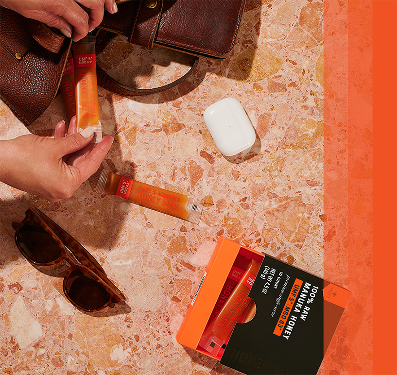 Manuka Honey Mini sticks placed on a marble surface alongside a bag, sunglasses, and AirPods.