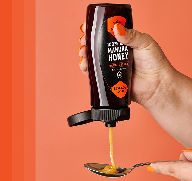 Manuka bottle being squeezed onto spoon with pink background.