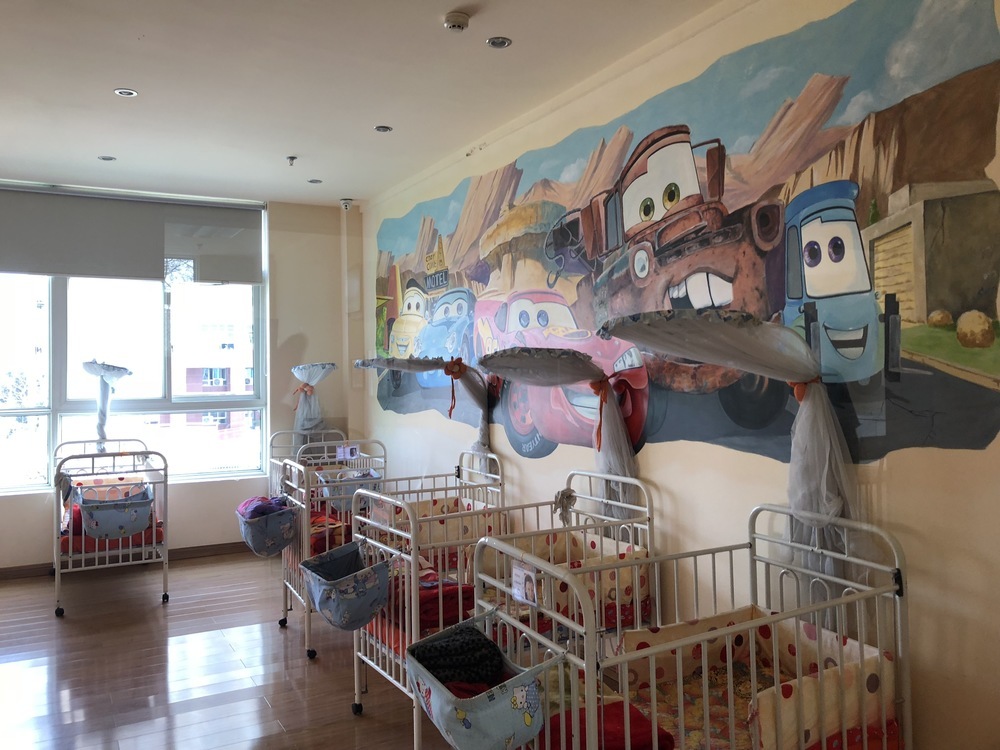 Children's room with cribs and a cartoon car mural on the wall.