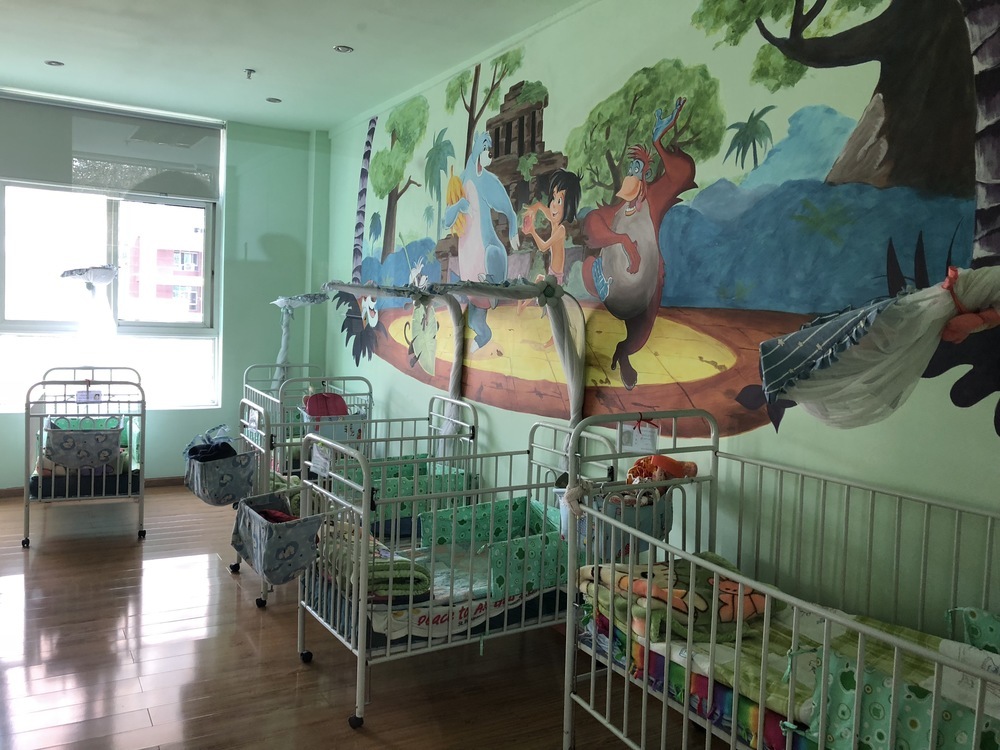 A nursery with colorful cribs and a large animal-themed wall mural.