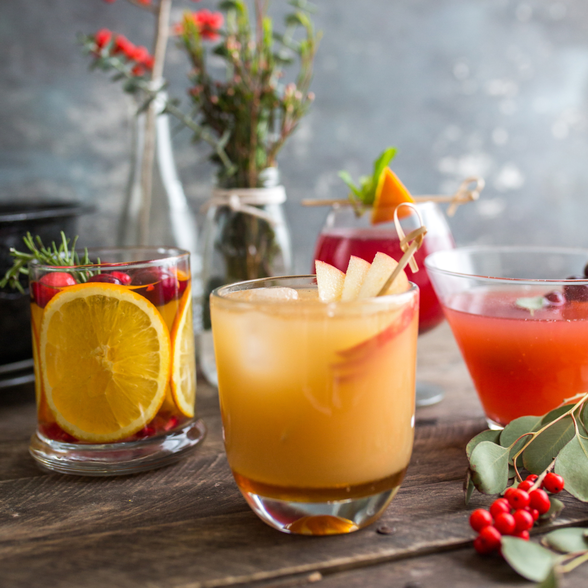 Beverages with fruit garnishes on wood with a hazy, cozy backdrop.