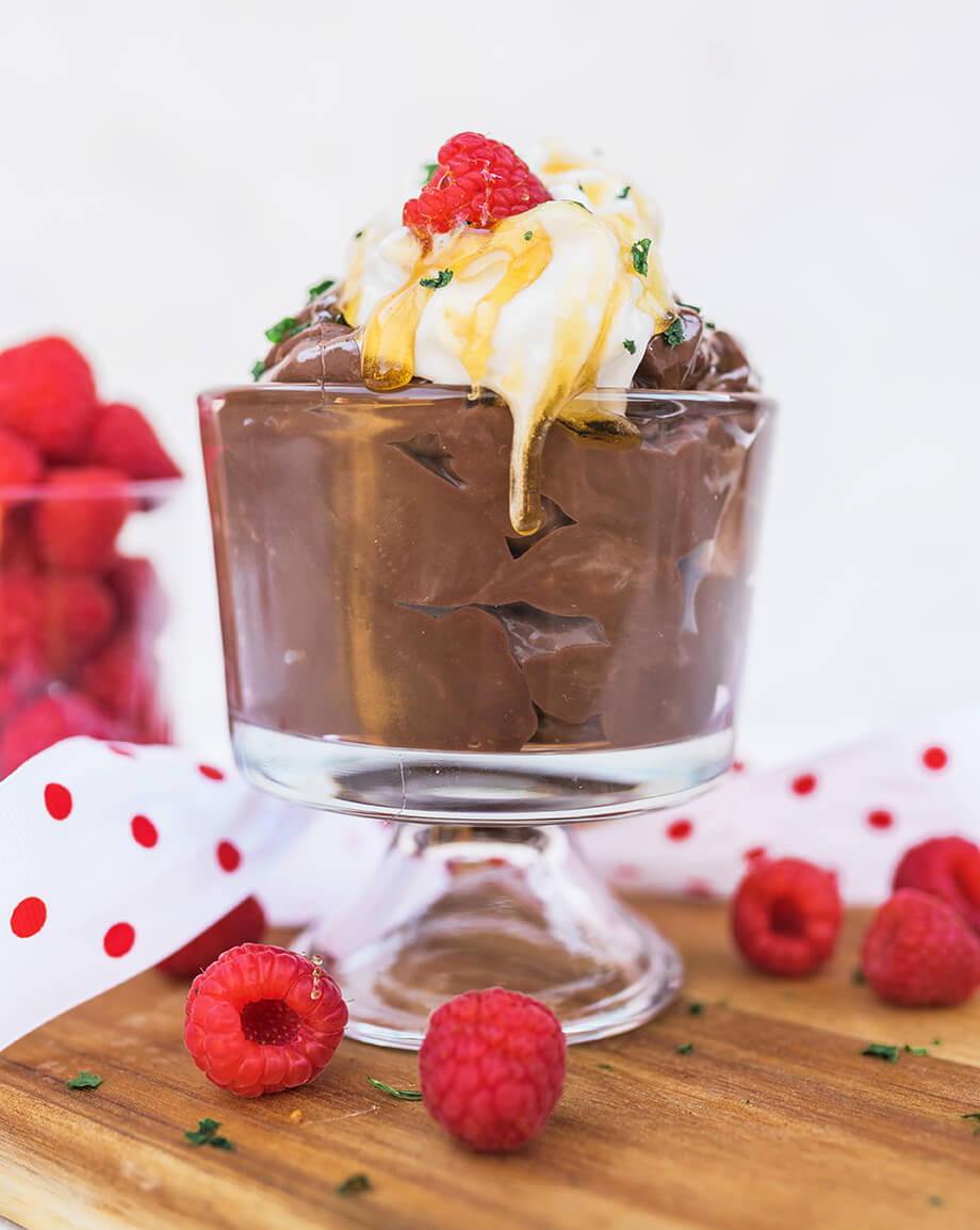 Chocolate mousse in a glass, topped with whipped cream, honey drizzle, and a raspberry.