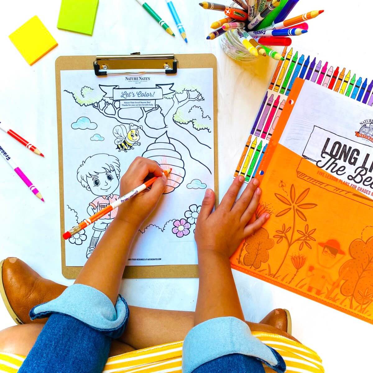 Child coloring a picture on clipboard with markers and colored pencils around.