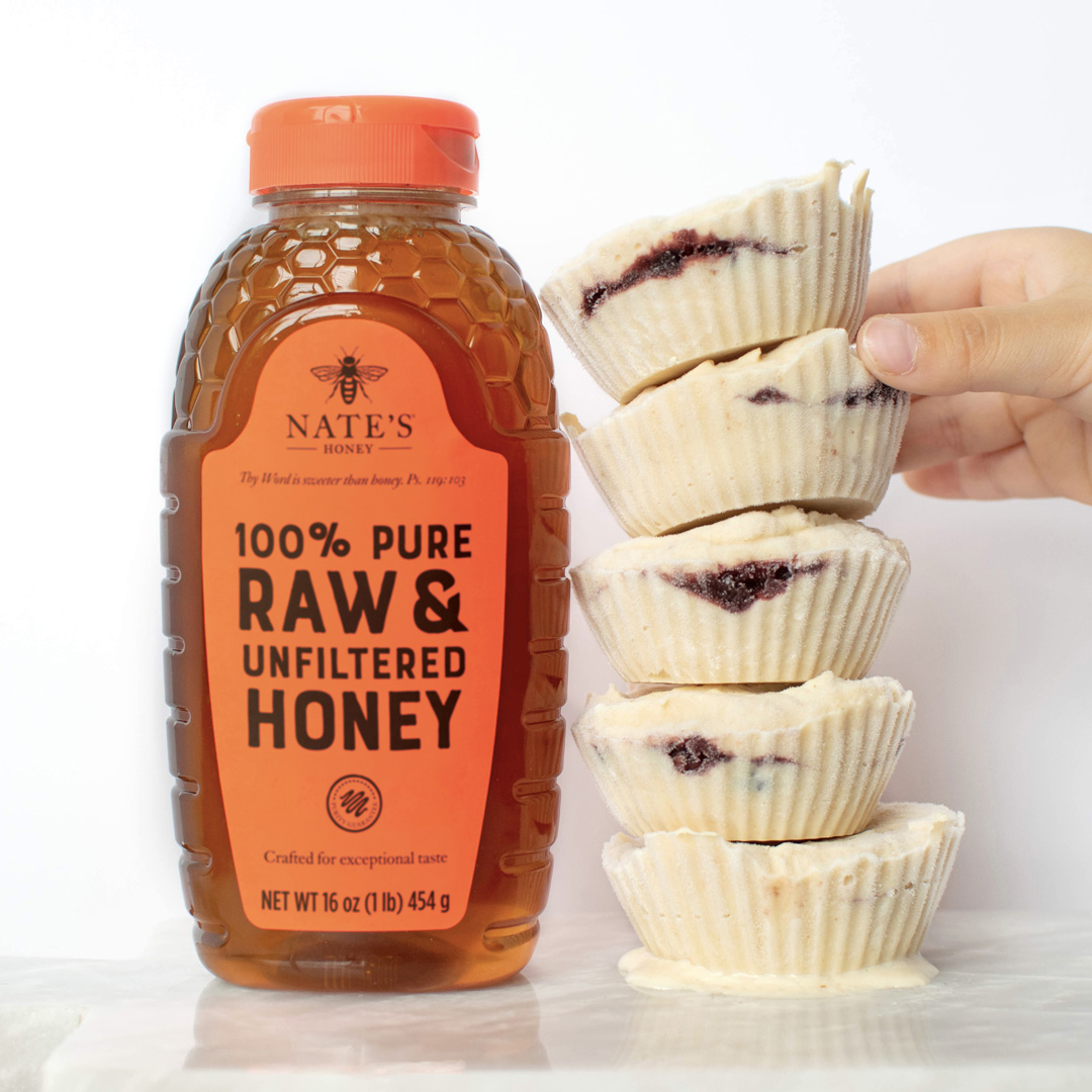 A hand stacking PB&J froyo bites next to a bottle of Nate's Honey against a white background.