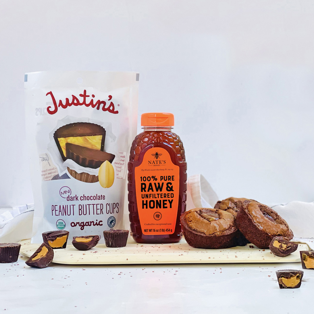 Bottle of Nate's Honey with Justin's Peanut Butter Cups and treats on a white background.