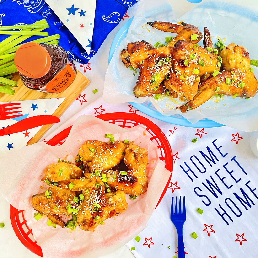 Honey-glazed Korean chicken wings on patriotic tableware with a bottle of Nate’s Honey and festive decorations.
