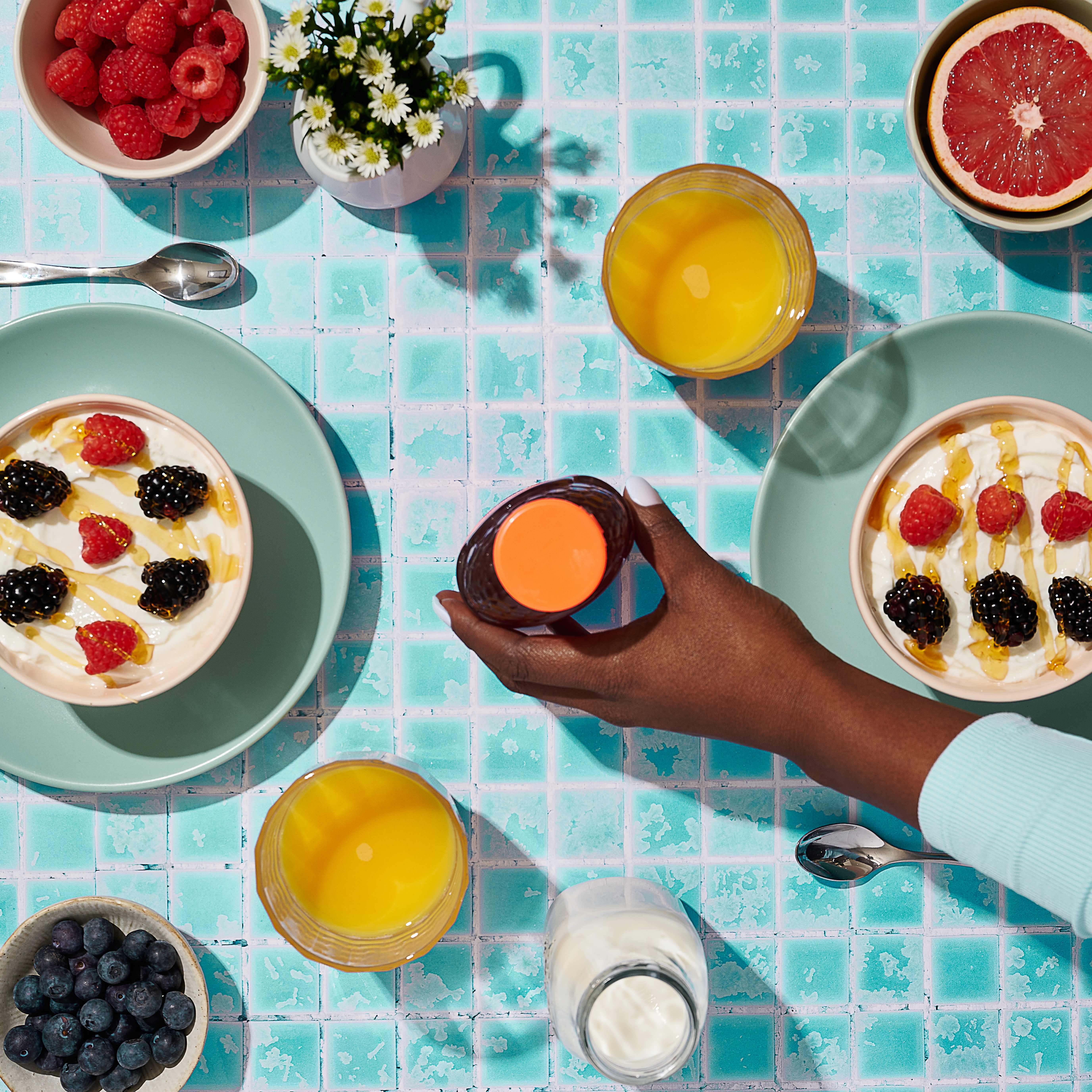 Hand holding Nate's Honey over a berry-topped yogurt bowl on a blue tiled table.