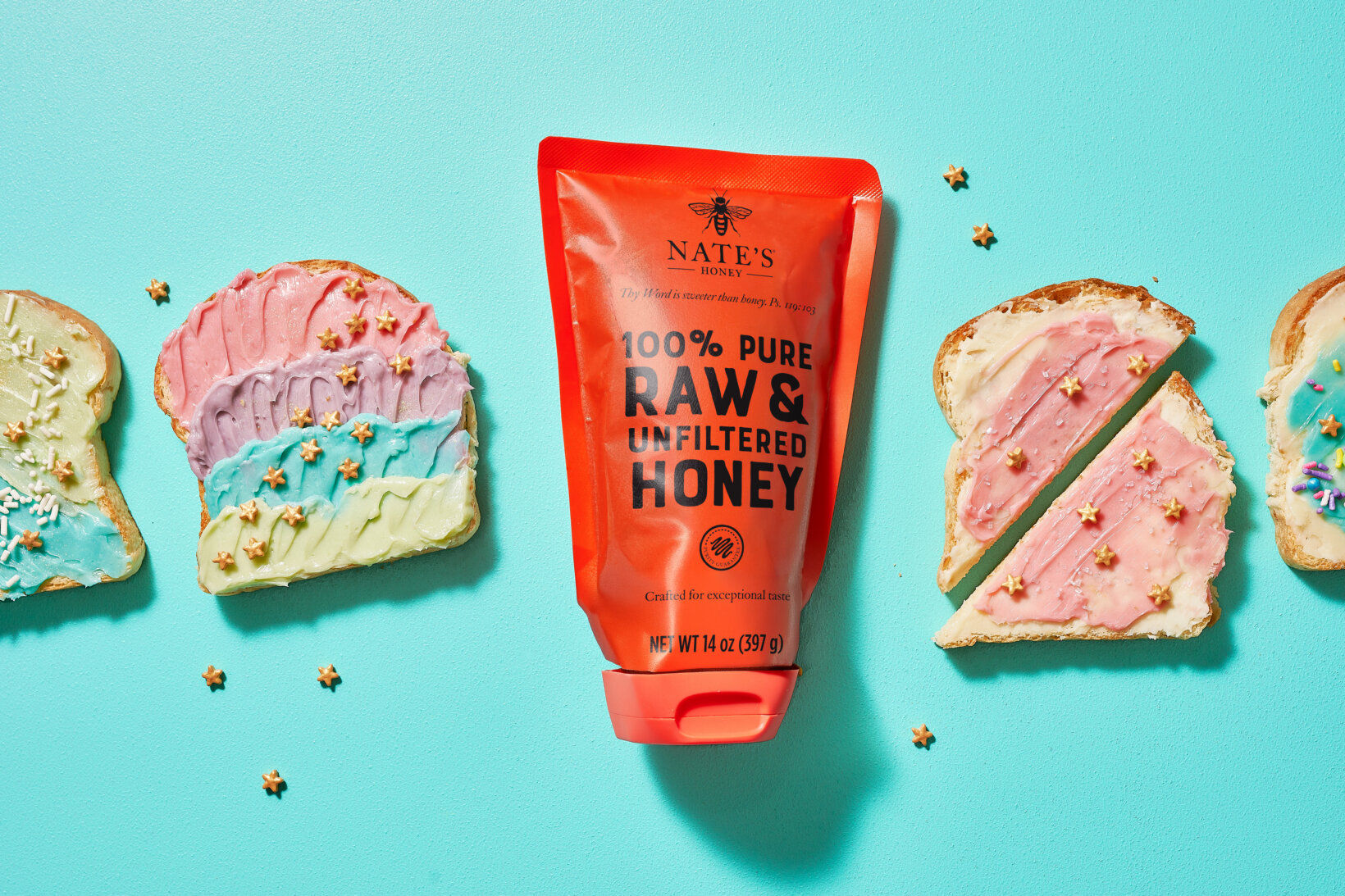 A tube of Nate's Honey next to slices of bread with colorful spreads on a blue background.