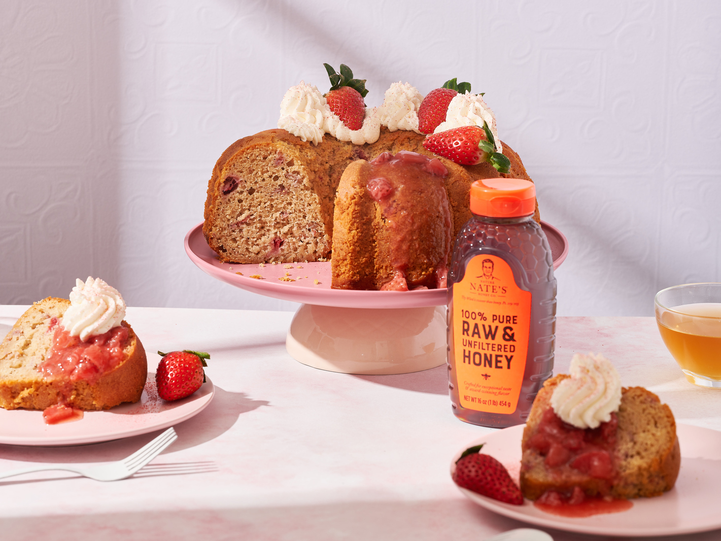 Strawberry cake slices on plates with honey bottle.